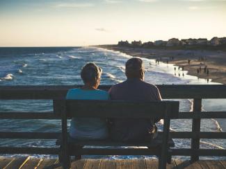 Married couple a bench staring at ocean.